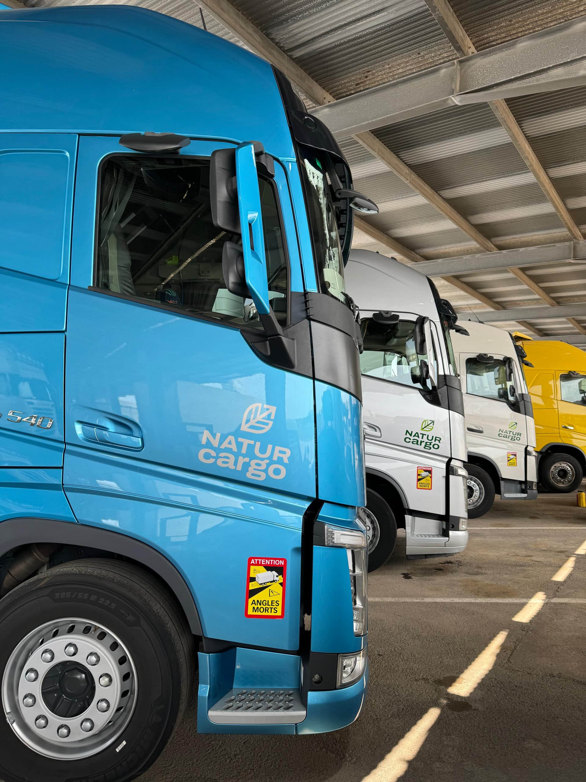 Camiones NaturCargo en almacén con camión azul destacado